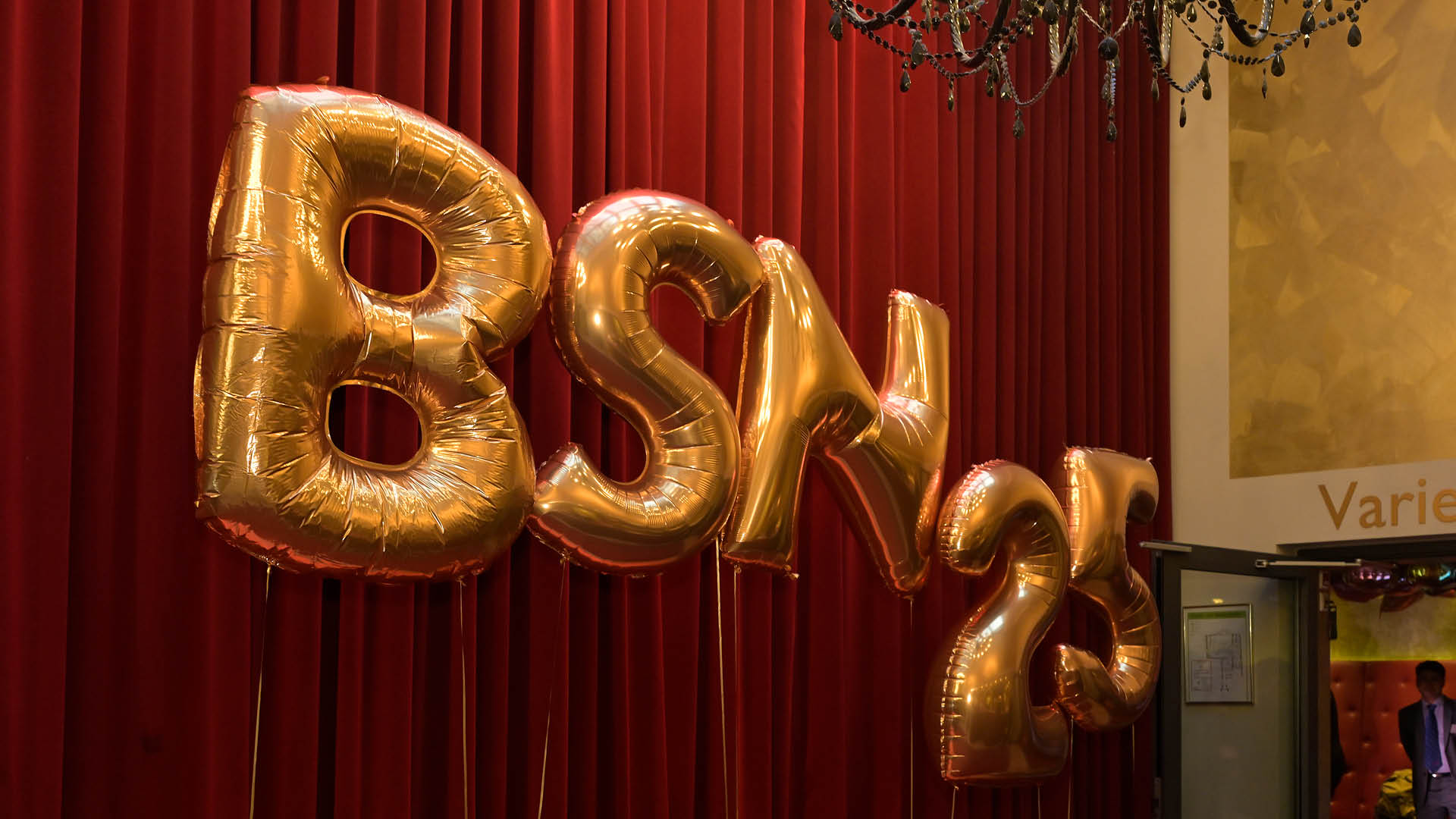 Bild von goldfarbenen Luftballons vor samtrotem B hnenvorhang, die den Schriftzug “BSN 25" zeigen.